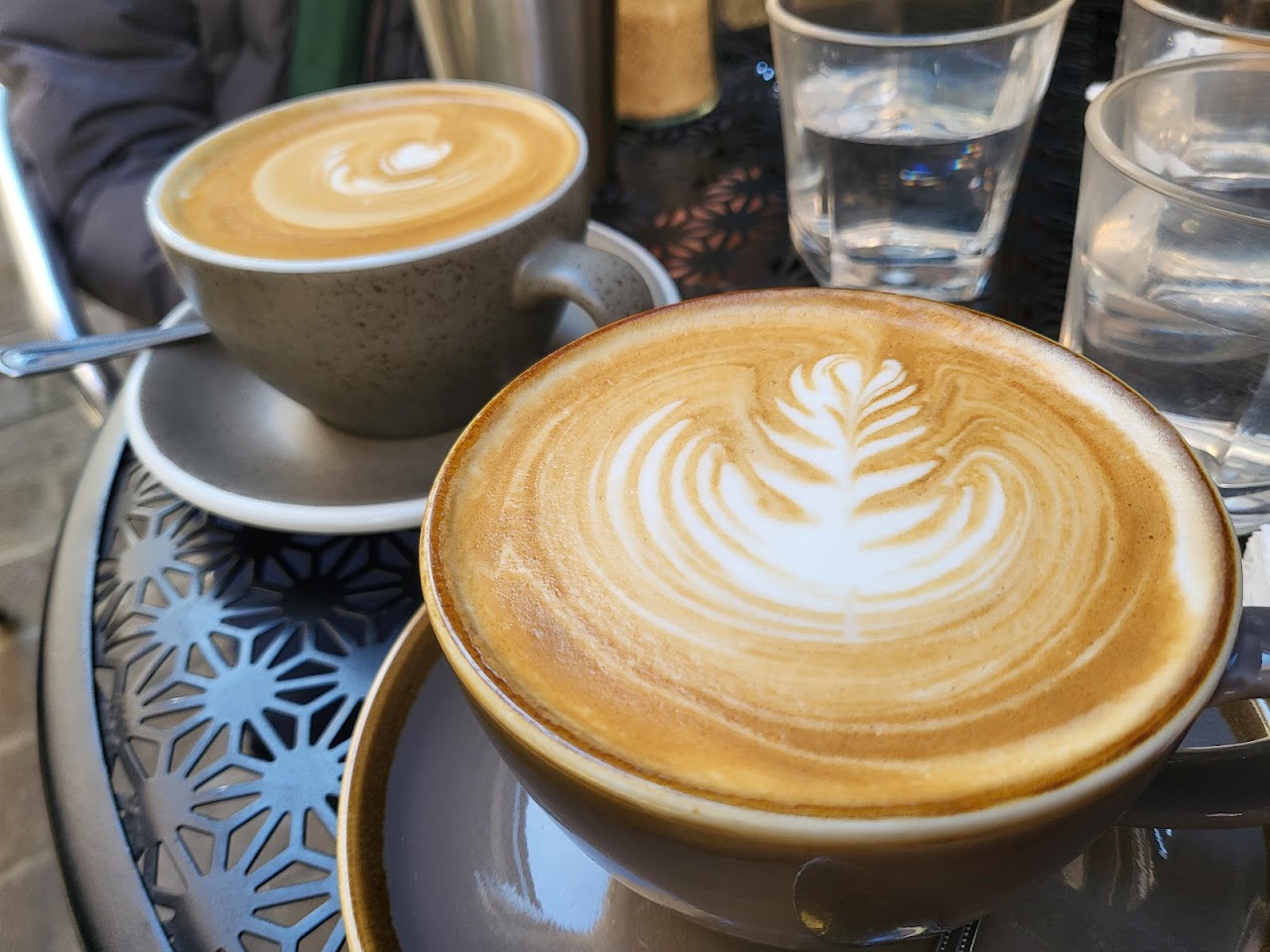 Two ASLAN coffees with latte art on an outdoor table